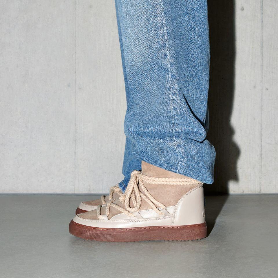 Buty marki INUIKII model Classic w kolorze beżowym na nogach osoby z niebieskich jeansach od boku.