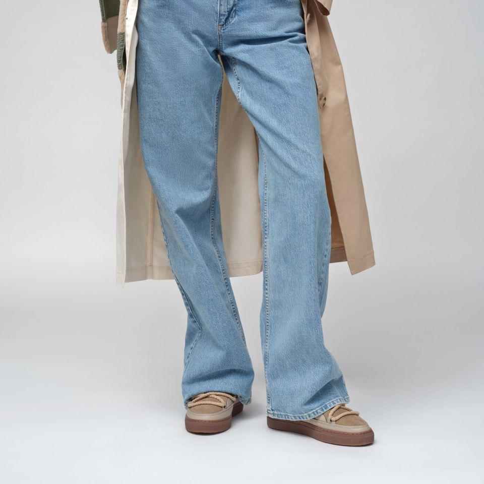 Buty marki INUIKII model Classic w kolorze beżowym na nogach osoby w niebieskich jeansach z przodu.