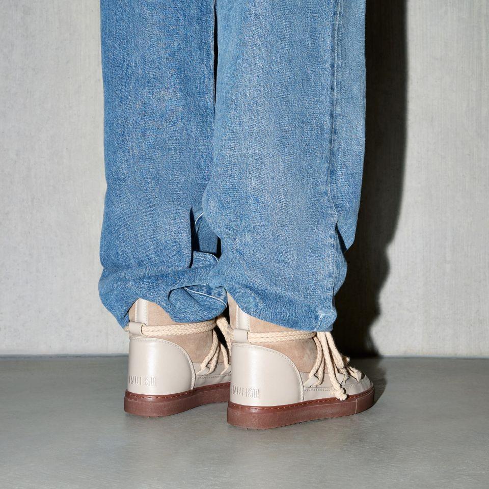 Buty marki INUIKII model Classic w kolorze beżowym na nogach osoby w niebieskich jeansach od tyłu.