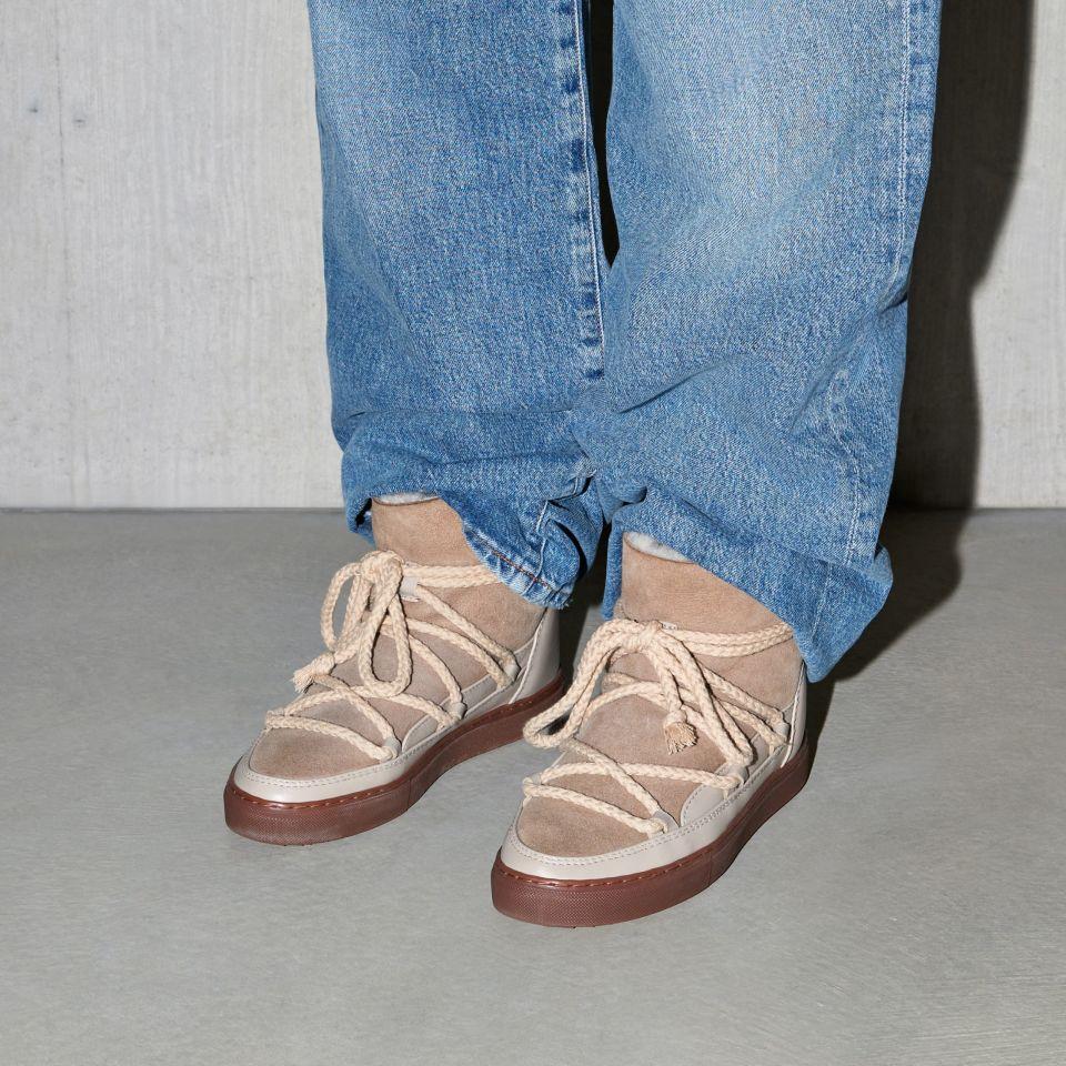 Buty marki INUIKII model Classic w kolorze beżowym na nogach osoby w niebieskich jeansach z przodu.